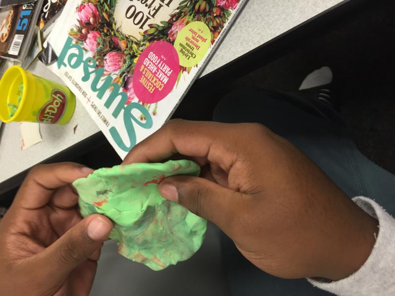 Image of teen's hand working with play-doh and magazine clippings 